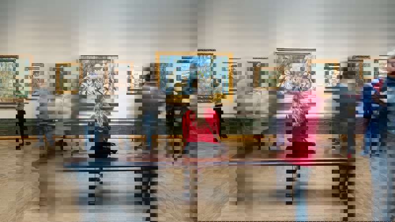 Timelapse Blur Of Woman Sitting On Bench Listening To Audioguide Looking At Painting